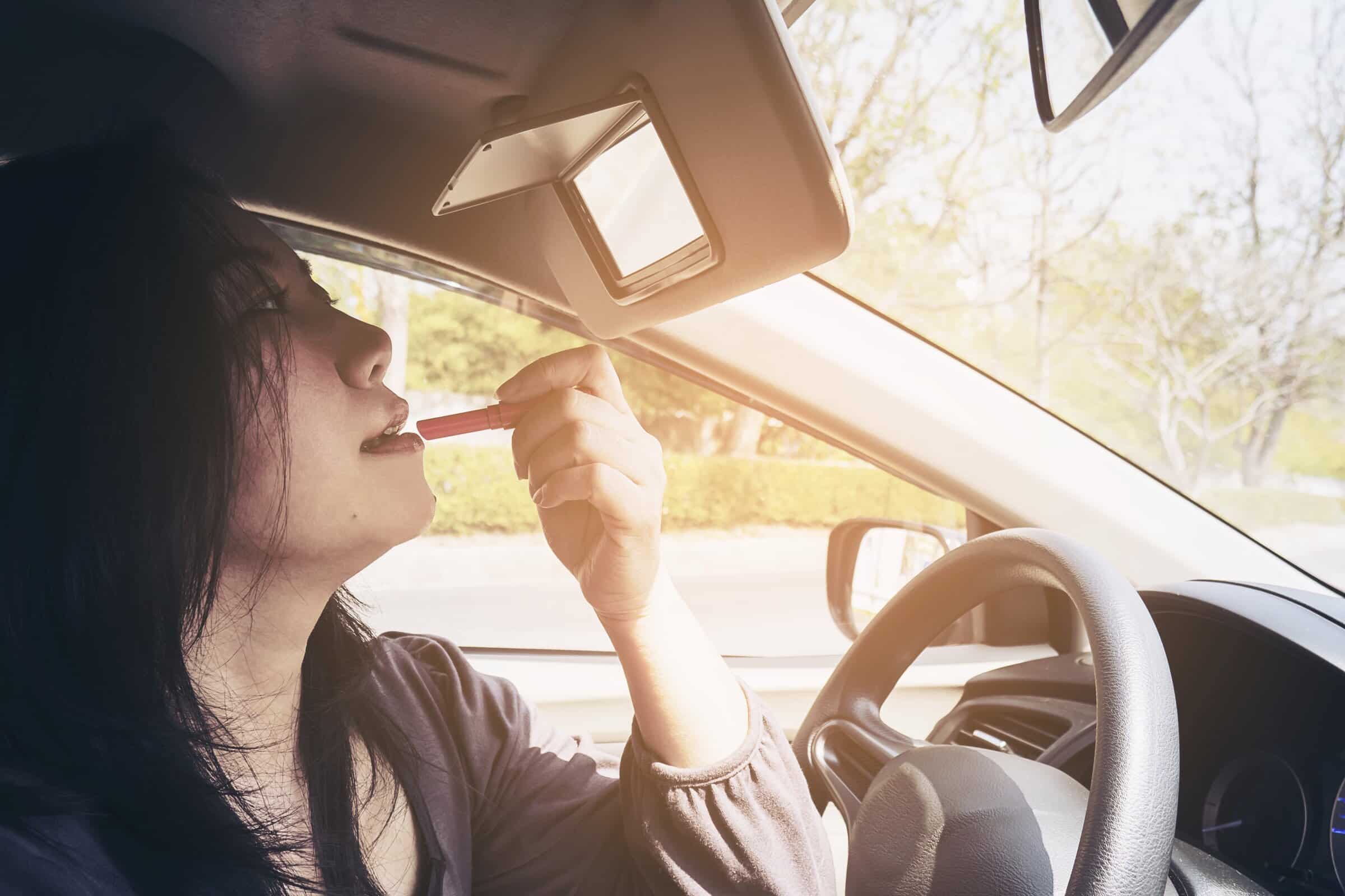 Woman making up her face using lipstick while driving car